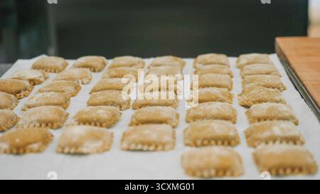 Carrés de pâtes aux raviolis crus fraîchement préparés disposés soigneusement sur du papier parchemin prêt pour la cuisson ou la congélation de délicieux plats italiens maison Preparatio Banque D'Images