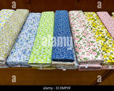 Divers rouleaux ou boulons de tissu floral indien à motifs soigneusement disposés sur une table d'affichage en bois dans un magasin. Banque D'Images