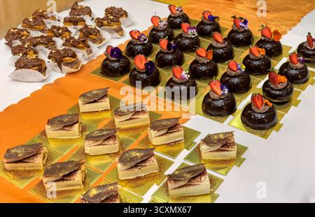 eclairs de chocolat, mousse de fraise, dômes, meringue, assis sur la table, flocons d'or comestibles en haut, enveloppés dans du papier Banque D'Images