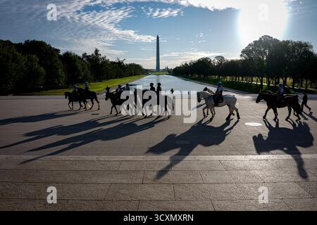 Washington DC, États-Unis. 15 octobre 2025. Une cavalcade policière passe devant le Washington Monument le matin, projetant de longues ombres sur le sol sous le soleil. Crédit : Kay Nietfeld/dpa/Alamy Live News Banque D'Images