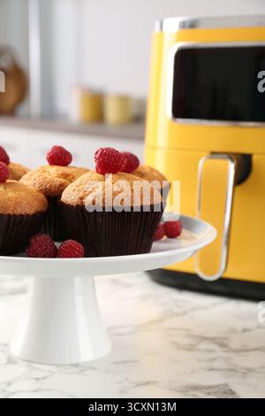 Muffins fraîchement cuits avec framboises et friteuse à air sur la table en marbre blanc dans la cuisine, gros plan Banque D'Images