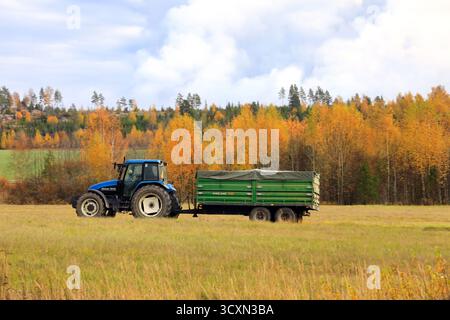 Conduite d'un tracteur agricole New Holland TS115 bleu et d'une remorque agricole Palms 150 verte dans un paysage automnal. Salo, Finlande. 13 octobre 2022. Banque D'Images