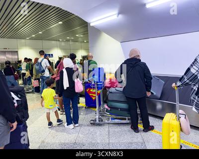 Les gens avec des bagages font la queue au carrousel à bagages de l'aéroport sous des lumières fluorescentes Banque D'Images