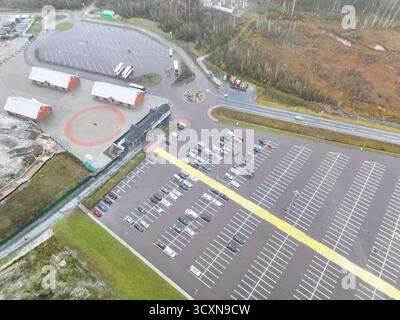 Vue aérienne aérienne d'un grand parking avec voitures, autobus et petits bâtiments de service à côté d'un paysage d'automne Banque D'Images