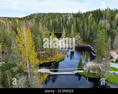 Vue aérienne d'une longue passerelle en bois traversant une rivière sombre entourée d'une dense forêt nordique aux couleurs automnales Banque D'Images