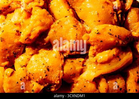 Gros plan de morceaux de poulet marinés assaisonnés pour pinchos morunos espagnols, enrobés d'un mélange orange vif d'épices et d'herbes sous une lumière chaude Banque D'Images