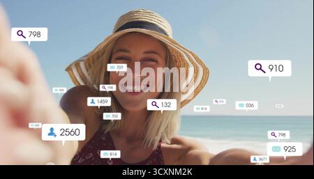 Femme portant chapeau de soleil de paille et maillot de bain prenant selfie avec smartphone sur la plage, avec des icônes numériques Banque D'Images