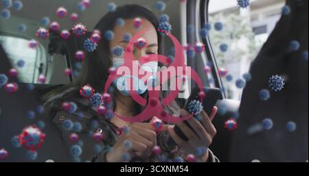 Tapotant femme smartphone portant un masque bleu dans le siège arrière de voiture, avec des graphiques rouges de biohazard et de virus Banque D'Images