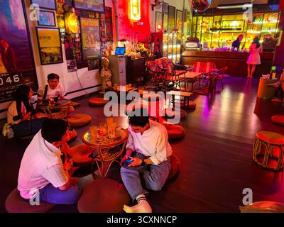 Bar secret caché confortable au thème rétro avec des néons vibrants clients asiatiques dégustant des boissons créant une ambiance chaleureuse kuala lumpur malaysia coussins de sol Banque D'Images
