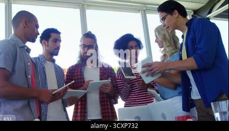 Collaboration six collègues tenant des tablettes et un ordinateur portable autour d'une table de conférence dans un bureau ensoleillé Banque D'Images