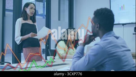 Présentation femme asiatique portant une tenue d'affaires à côté de la table dans le bureau en verre, avec des graphiques numériques Banque D'Images