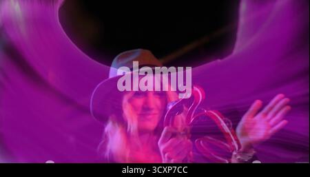 Musicien jouant portant un chapeau à large bord sur la scène de club secouant le tambourin sous les traînées de LED violettes Banque D'Images