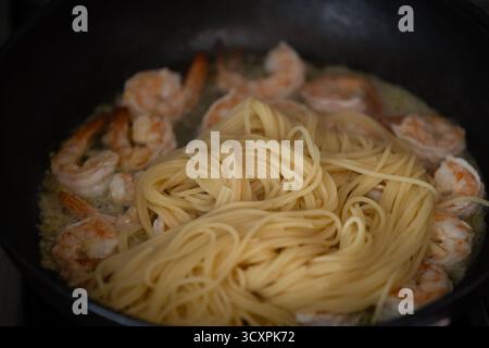 Gros plan de spaghettis fraîchement cuits aux crevettes dans une sauce crémeuse, servis dans une poêle. Banque D'Images
