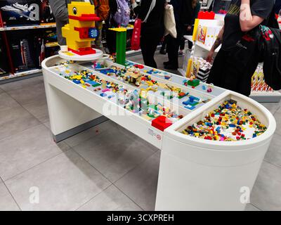 Manchester, Royaume-Uni - 26 septembre 2025 : briques Lego colorées dispersées sur une table blanche moderne dans une exposition de magasin de jouets animée. Banque D'Images