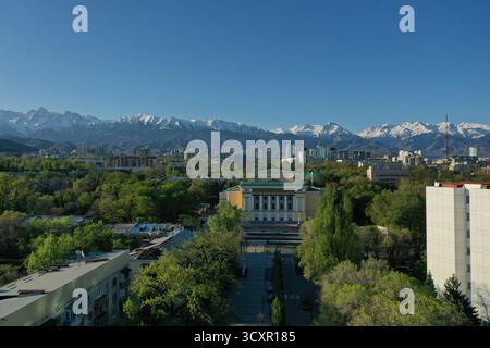 Panorama urbain d'Almaty mettant en valeur l'opéra abay dans un cadre de parc verdoyant, avec des bâtiments modernes contre les sommets enneigés des montagnes tian shan und Banque D'Images
