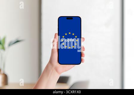 Smartphone tenant dans la main affichant le drapeau de l'Union européenne et le logo GDPR symbolisant la protection des données, le droit à la vie privée et la réglementation numérique européenne Banque D'Images