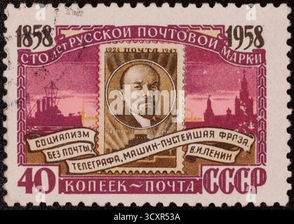 Un timbre-poste soviétique représente un portrait de Lénine entouré de texte et d'images symboliques, y compris des navires et des bâtiments, dans des tons violets, roses, Banque D'Images