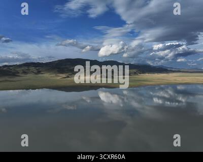 Vaste paysage montagneux avec un lac calme reflétant parfaitement les nuages spectaculaires au-dessus de la tête et le ciel bleu vif, créant un cadre serein et tranqu Banque D'Images