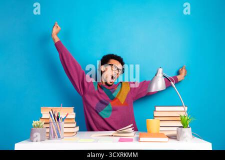 Homme drôle s'étirant au bureau avec un fond bleu vif et un pull décontracté stylé dans un environnement d'apprentissage détendu Banque D'Images