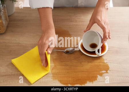 Femme essuyant avec un chiffon le café renversé sur la table dans la cuisine, gros plan Banque D'Images