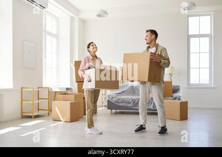 Couple heureux portant des boîtes en carton tout en emménageant dans un nouvel appartement lumineux Banque D'Images