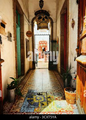 Couloir d'entrée dynamique avec des carreaux décoratifs et des portes colorées menant à un coin salon extérieur avec une décoration crâne traditionnelle Banque D'Images