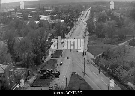 Une photo d'archives panoramique des années 1980 montre la vue depuis la jonction des rues Karla Marksa (aujourd'hui Tsentralna) et Yunykh Kommunarov (aujourd'hui Bankivska) à Sloviansk. La longue artère droite est animée par la circulation quotidienne, y compris un trolleybus articulé classique. Cette image illustre parfaitement l'ampleur du réseau de transports publics de la ville et le rythme quotidien d'un grand centre industriel. C'est un précieux document historique de l'environnement urbain dans un Donbass pacifique avant la guerre Banque D'Images