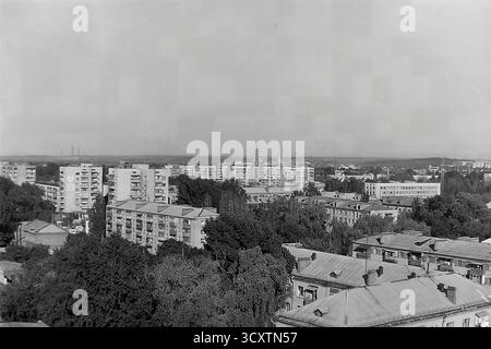 Une photo d'archives à grand angle des années 1980 capture le vaste paysage urbain de Sloviansk, en République socialiste soviétique d'Ukraine. La vue sur la jonction des rues Oktyabrskoy Revolyutsii (aujourd'hui Vasylivska) et Yunykh Kommunarov (aujourd'hui Bankivska) révèle une riche tapisserie de l'histoire de la ville. Les toits plus anciens au premier plan laissent place à de nouveaux immeubles d'appartements de l'ère soviétique et à une ligne d'horizon industrielle au loin. Il s'agit d'un témoignage précieux de l'évolution de l'environnement urbain d'un Donbass pacifique avant la guerre Banque D'Images