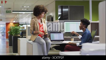 Discuter de deux collègues travaillant dans un bureau ouvert partageant occasionnellement des données sur tablette et ordinateur portable Banque D'Images