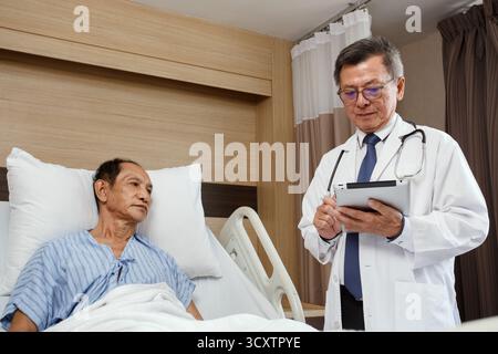 Patient cancéreux âgé allongé sur le lit d'hôpital parlant avec le médecin tenant un comprimé. consultation médicale et bilan médical en chambre d'hôpital, pro Banque D'Images