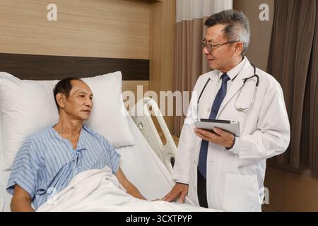 Patient cancéreux âgé allongé sur le lit d'hôpital parlant avec le médecin tenant un comprimé. consultation médicale et bilan médical en chambre d'hôpital, pro Banque D'Images