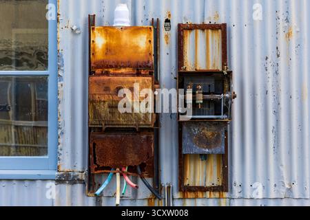 Vieux panneaux électriques triphasés rouillés sur un mur métallique altéré dans les anciens chantiers navals de Cockatoo Island, Sydney, Australie Banque D'Images