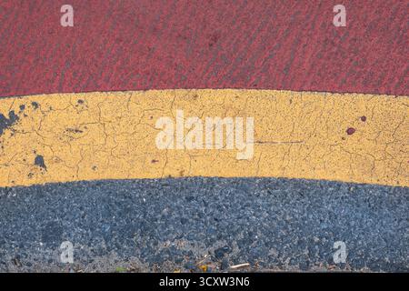 Texture de route goudronnée grise avec peinture rouge et jaune Banque D'Images