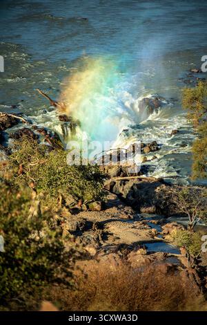 Un arc-en-ciel de lumière passant à travers le jet du canal principal des chutes d'Epupa depuis le point de vue Banque D'Images