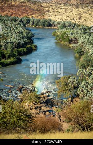 Un arc-en-ciel de lumière passant à travers le jet du canal principal des chutes d'Epupa depuis le point de vue Banque D'Images