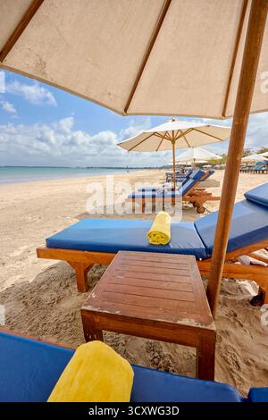 Une rangée de chaises longues avec des serviettes roulées sous des parasols sur Jimbaran Beach par une journée nuageuse. Kuta Sud, Badung, Bali, Indonésie. Banque D'Images