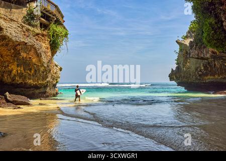 Surfeur va dans l'eau à Uluwatu Beach (Blue point Beach), pittoresque plage de sable isolée entourée de falaises. Pecatu, Badung, Bali, Indonésie. Banque D'Images