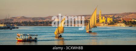 Feluccas (bateaux à voile égyptiens traditionnels) sur le fleuve Nil au coucher du soleil à Assouan, Egypte tête de voyage panoramique Banque D'Images