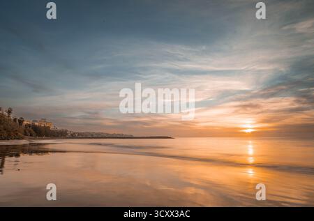Le soleil se lève à l'horizon, peignant la plage de Gran Canaria dans des tons dorés. Les vagues douces reflètent la lumière chaude du matin, créant un coasta serein Banque D'Images