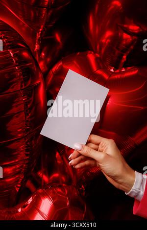Main tenant la carte vierge contre des ballons rouges en forme de coeur Banque D'Images