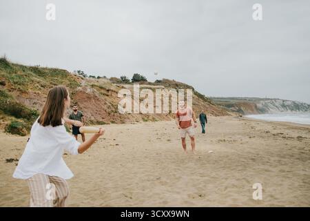 Une femme joue au baseball avec un homme et deux autres personnes sur une plage. La femme tient une batte et l'homme tient une balle. La scène est Lighthearte Banque D'Images