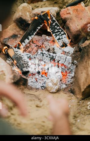 Une personne se tient debout au-dessus d'un foyer avec un tas de bois et un rocher. Le feu brûle avec éclat et la personne le regarde Banque D'Images
