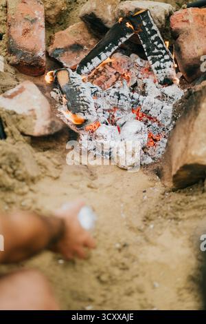 Une personne se tient debout au-dessus d'un foyer, tenant une boîte de fluide plus léger. Le feu brûle avec éclat, et la personne se prépare à l'allumer. La scène Banque D'Images