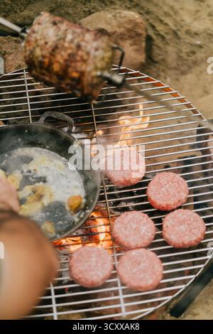 Une personne fait cuire des hamburgers sur un gril. Les hamburgers sont sur une grille métallique et sont cuits sur une flamme nue Banque D'Images