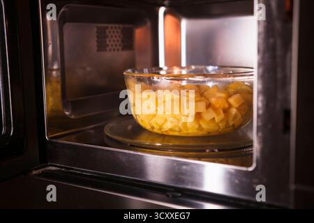 Mettre un bol avec des pommes de terre pelées crues au micro-ondes. Cuisiner à la maison. Nourriture maison fraîche. Banque D'Images