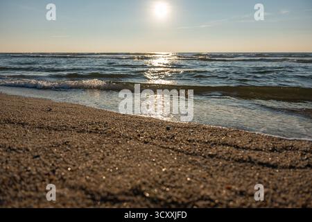 La lumière dorée du soleil scintille sur les douces vagues de la mer le long d'une plage de sable. L'horizon brille doucement sous le ciel du soir. Banque D'Images