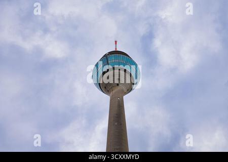 Emblématique tour de télécommunications Rheinturm vole contre ciel bleu nuageux à Düsseldorf, Allemagne - site urbain et attraction touristique vu de B. Banque D'Images