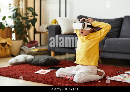 Une fille profite d'une expérience immersive dans son salon confortable tout en portant un casque VR. Banque D'Images