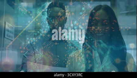 Examen de collègues examen de documents imprimés au bureau, avec moniteurs, murs en verre, superposition Banque D'Images