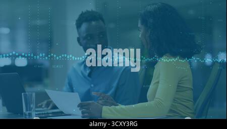 Examen des documents par une femme et un collègue masculin à la table de bureau, avec ordinateur portable et graphique numérique Banque D'Images